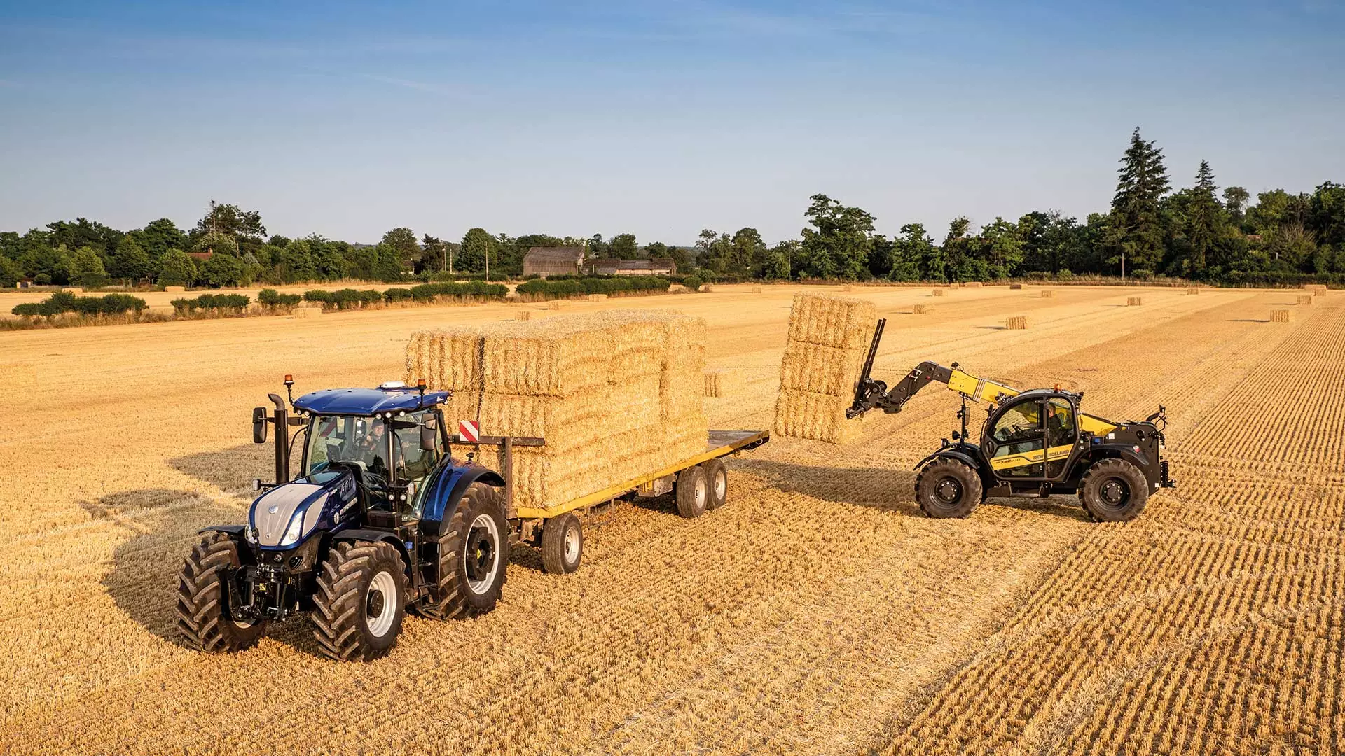 New Holland compact telehandler TH in action loading straw bales onto a trailer in a harvested field.