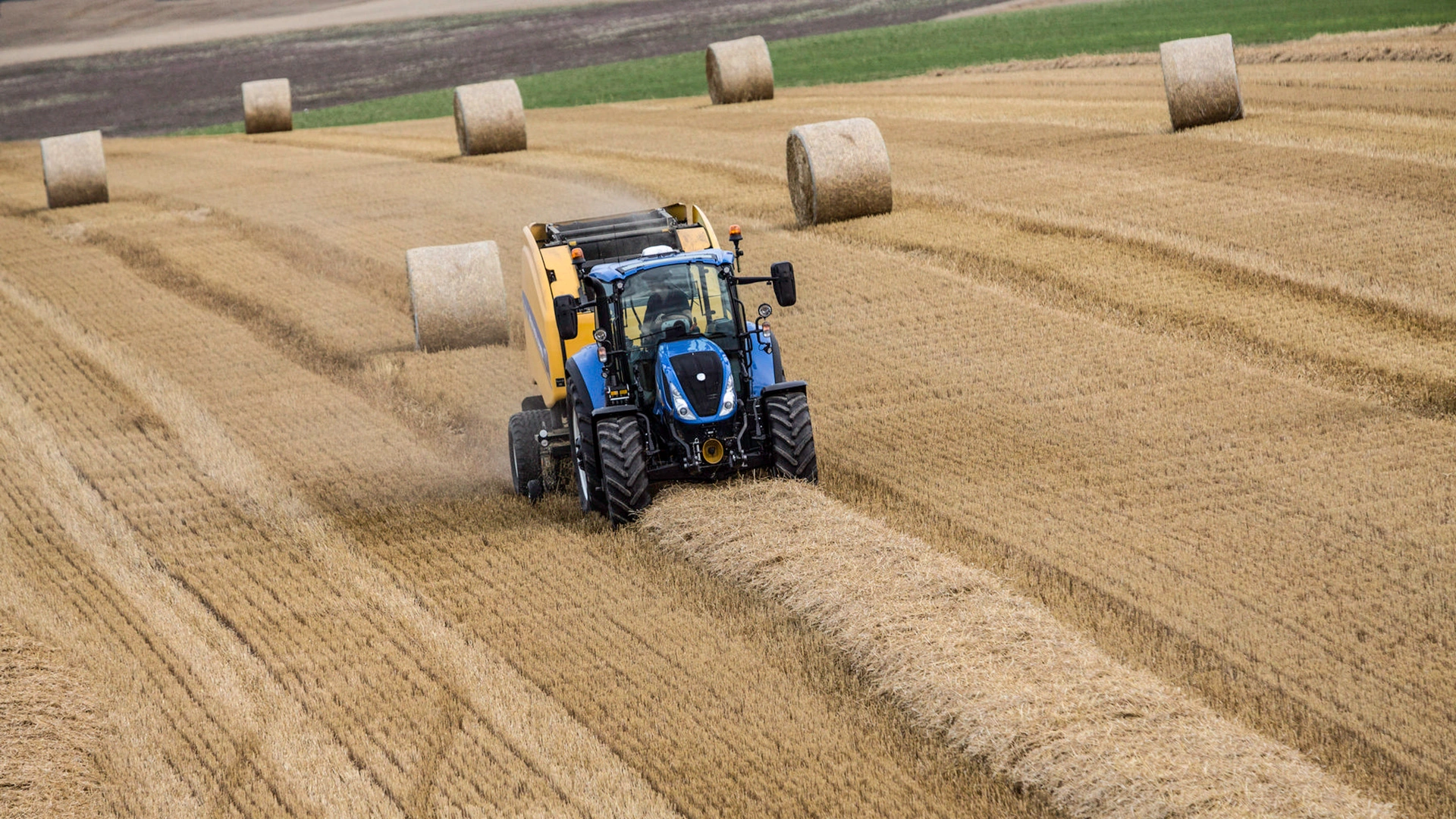 Tractor and Roll-Belt round baler combination actively bundling hay on the farmland