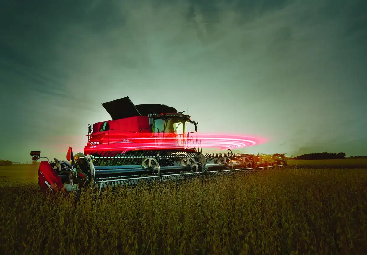 Red CASE IH combine harvester in a field at dusk with a swirling pink light effect around its middle.