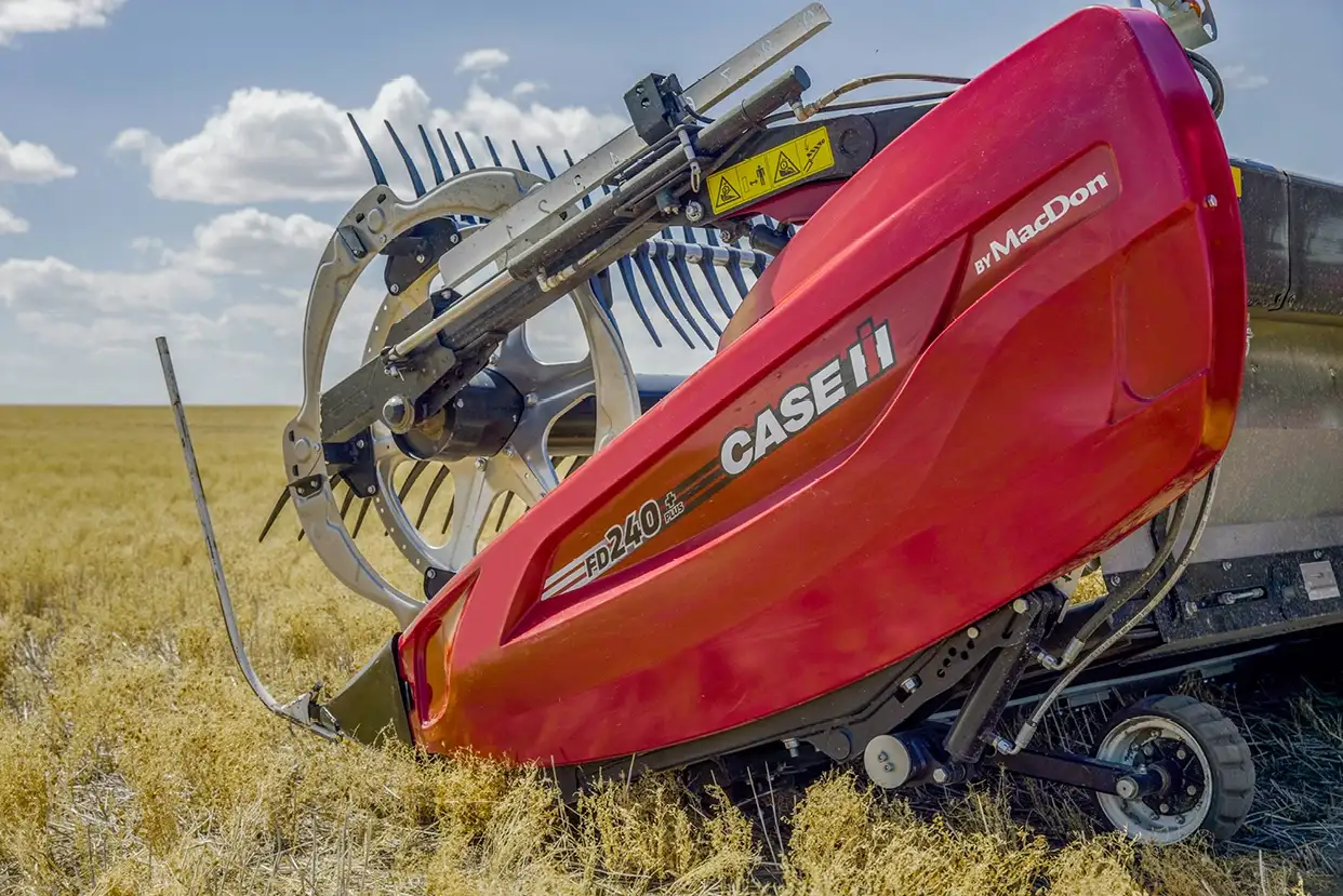 Red Case IH FD240 grain header in a golden field under a blue sky with clouds. 