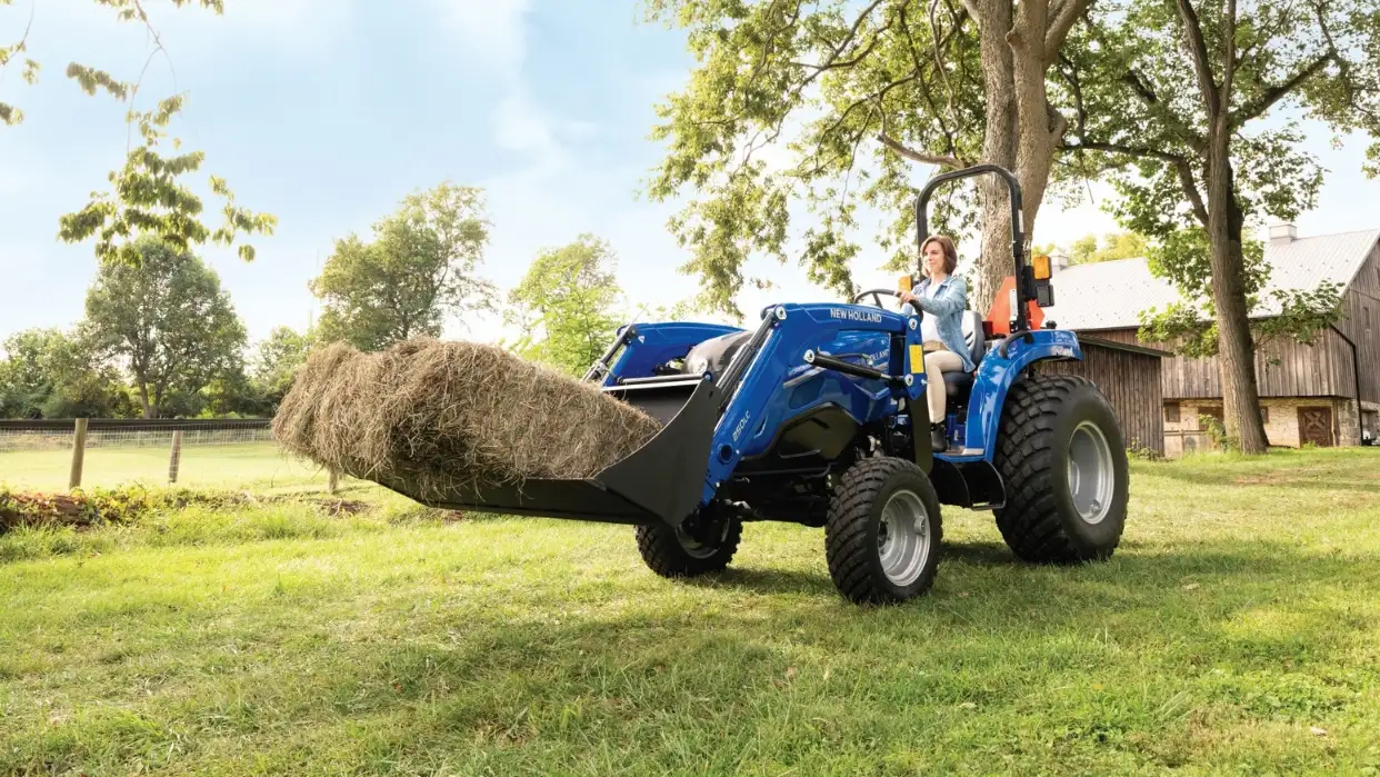 Woman transporting hay bale with tractor.