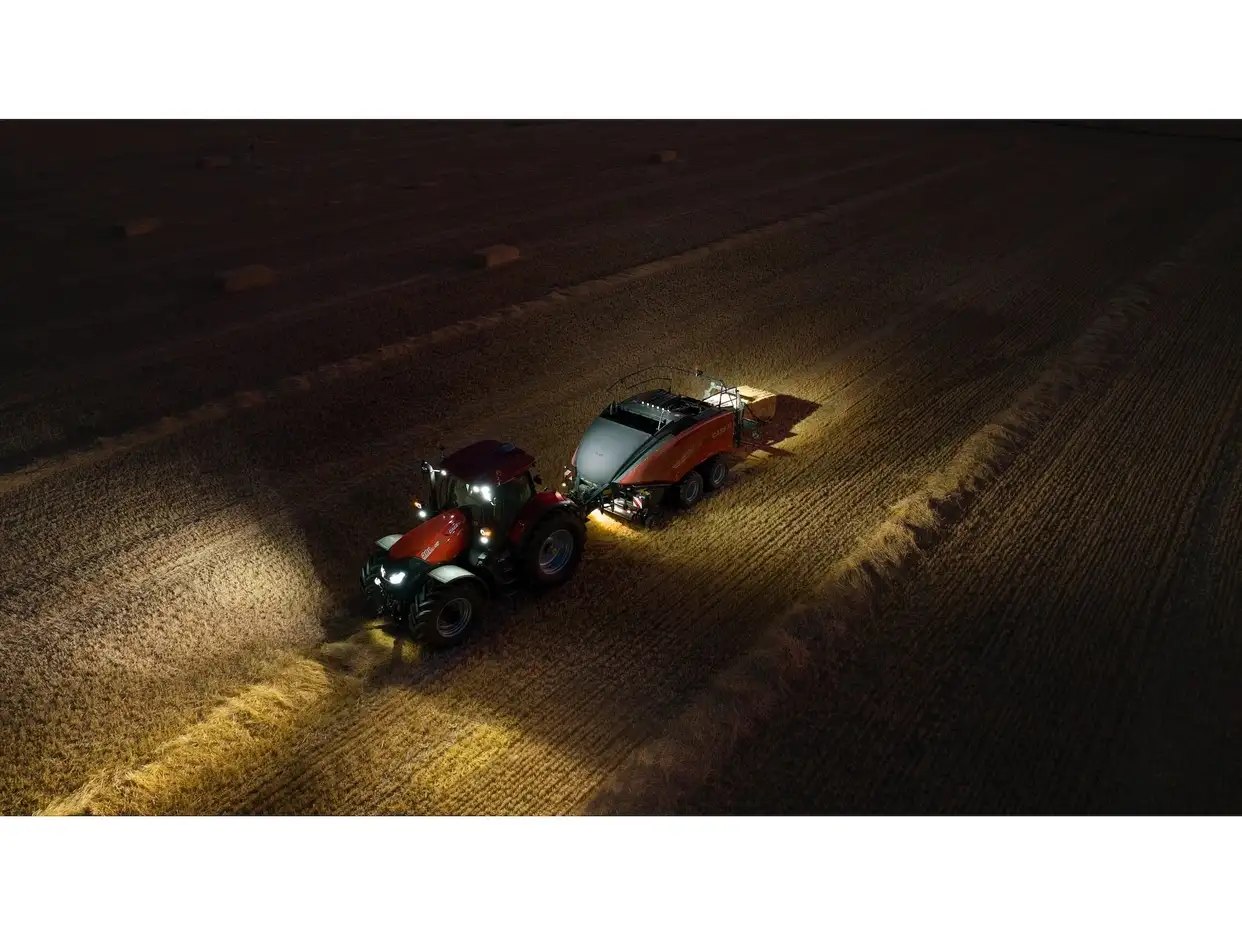 Aerial night view of a Case IH tractor with LB424 XL large square baler working in a stubble field with lights on