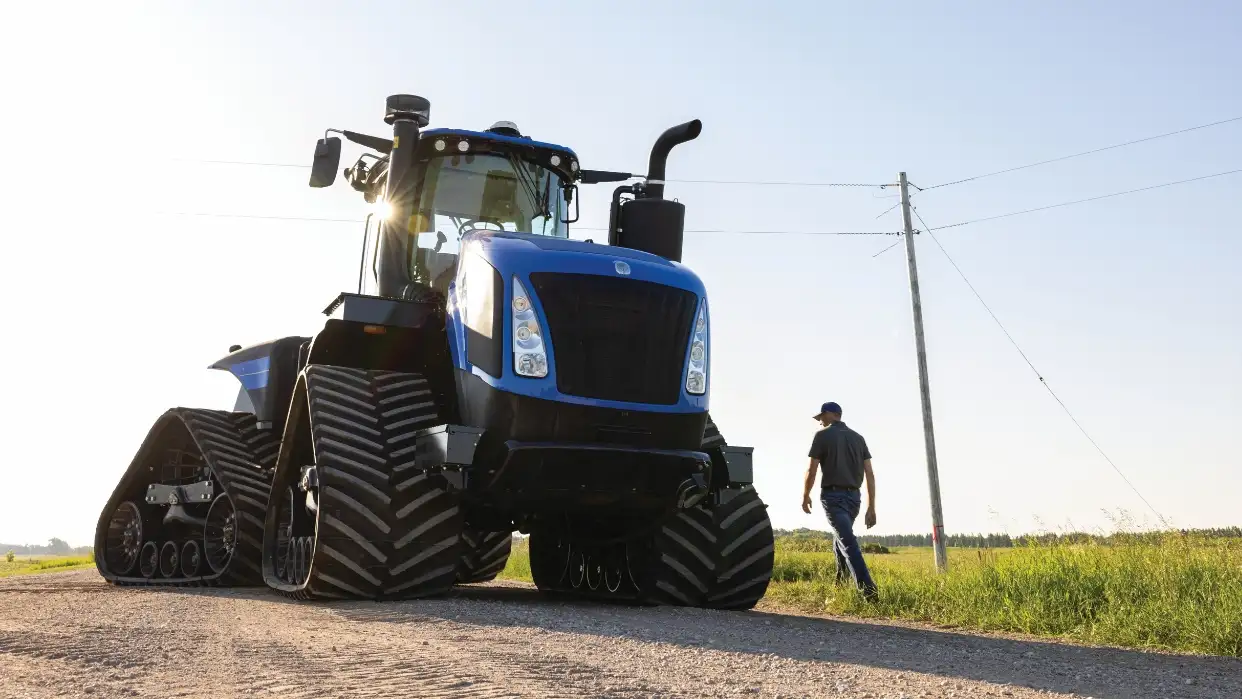 Man walks next to a big blue tractor on a gravel road.