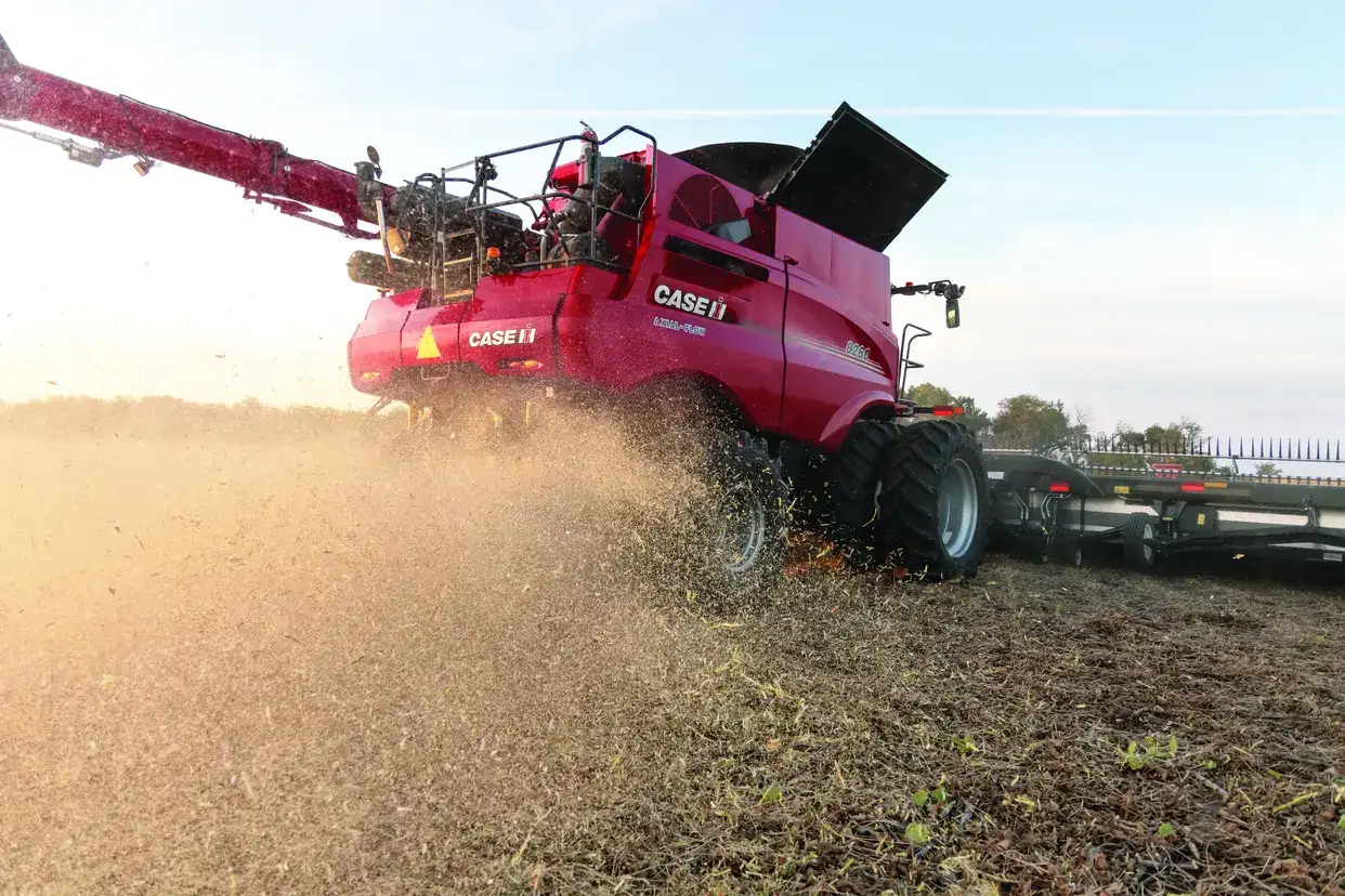 A red combine Case IH harvester operates in a golden field, harvesting crops under a clear blue sky.