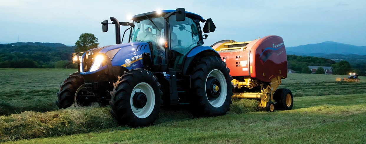 T6 Series tractor pulls a baler at dusk