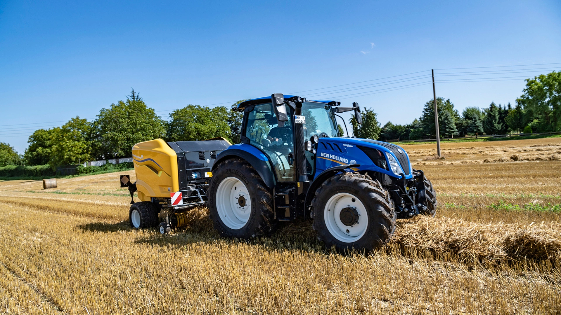 New Holland T5 tractor with a Roll Baler 125 in a harvested wheat field.