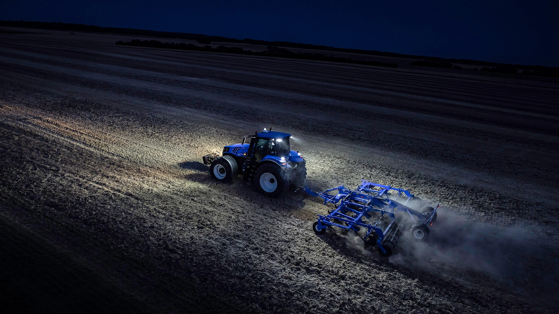 T8 Genesis tractor tilling soil in an expansive agricultural field during the night