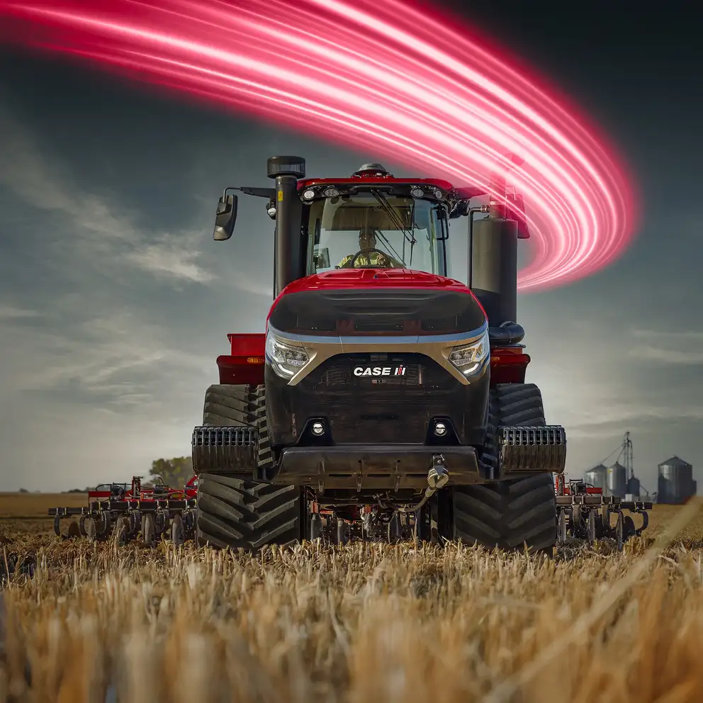 Front view of a red Case IH tractor in a field with pink light streaks swirling above against a cloudy sky.