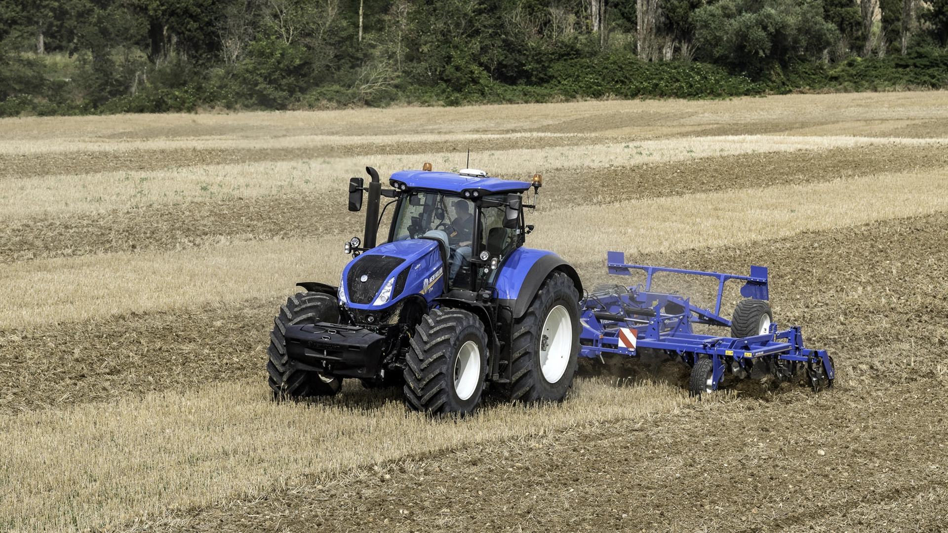 Working farm scene with tractor and mounted stubble cultivator equipped with rigid tine cultivator and cage rollers