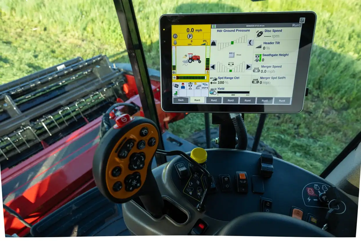 Inside a modern Case IH farm machine cab, a touchscreen displays harvesting data beside steering controls and red equipment in a sunny field.