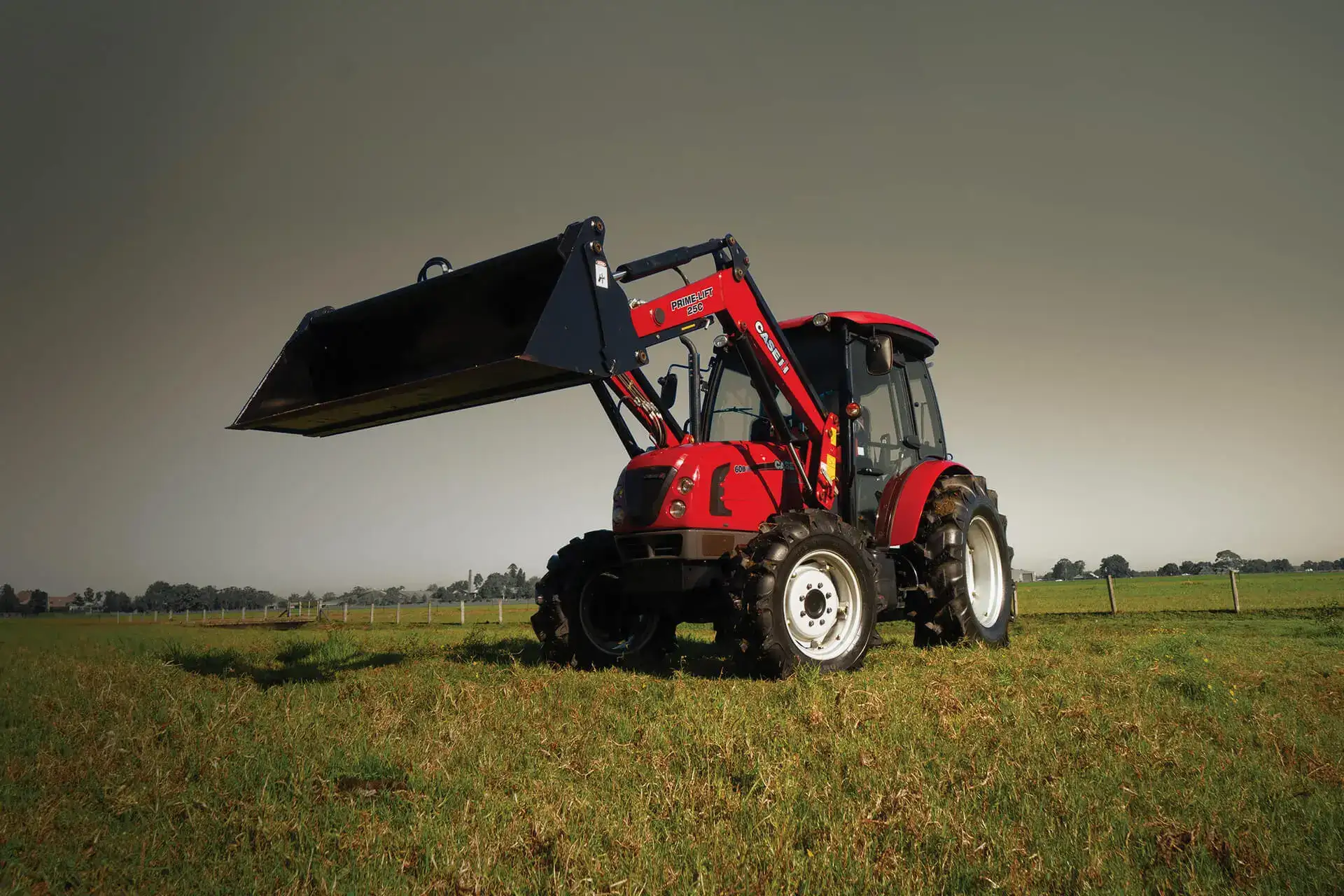 Red Case IH tractor sitting in farm on field with attachment bucket