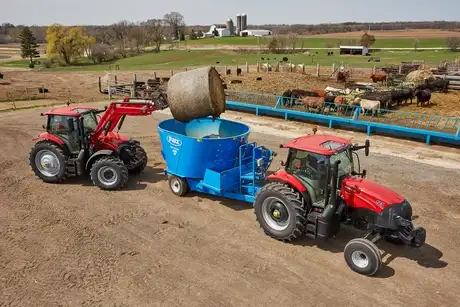 Two Maxxum tractors transporting hay on a farm.