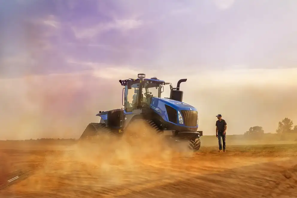 New Holland T9 tractor with person standing next to it in the dust