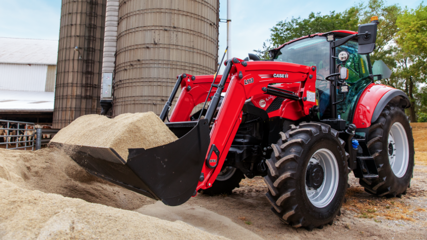 A Case IH tractor with a front loader is scooping sand near large silos on a farm.