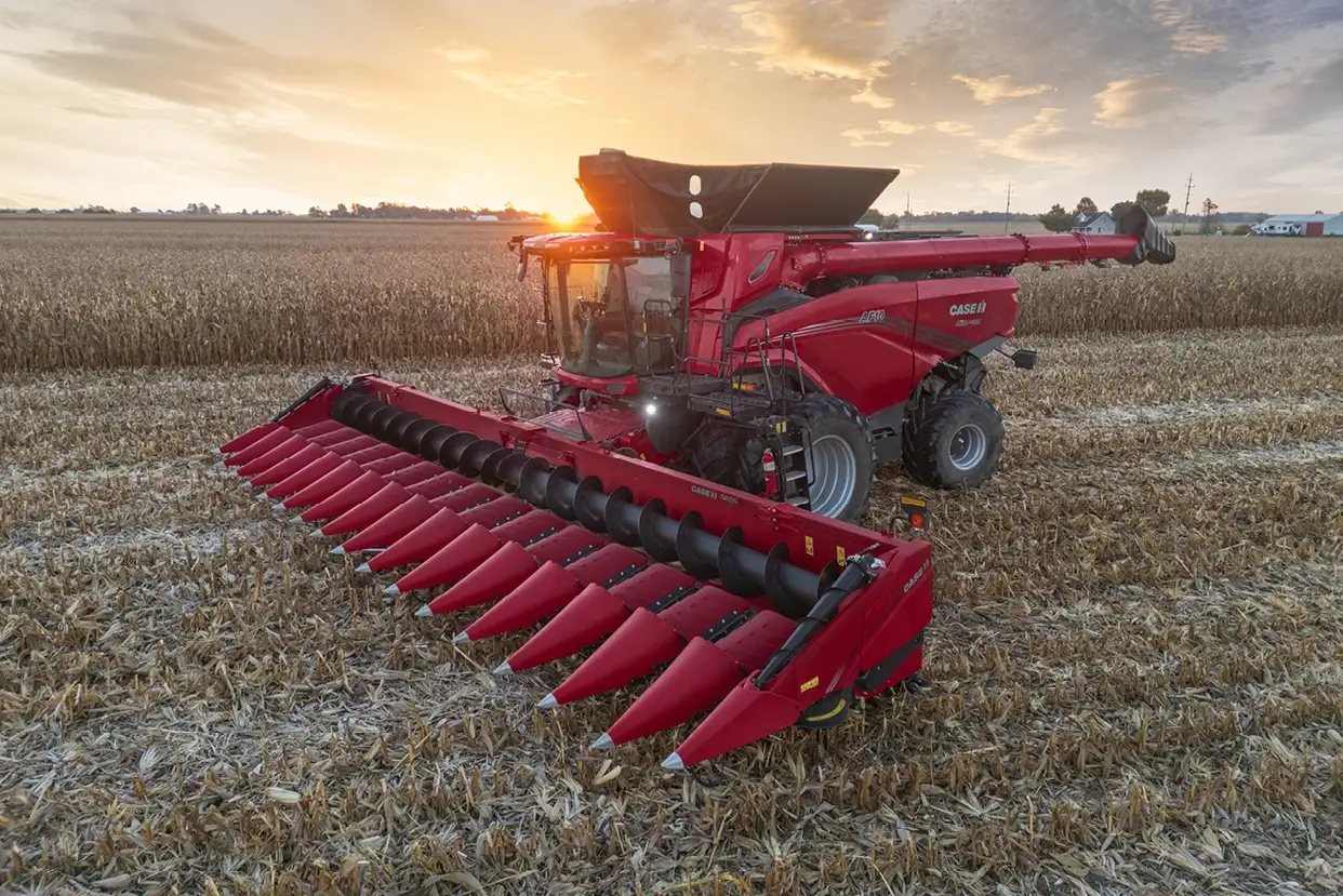 A Case IH C500 series combine harvester works through a cornfield at sunset, casting warm light over the machine and field, with scattered clouds enhancing the serene scene.