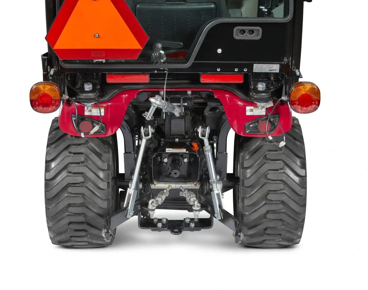 Rear view of a Case IH subcompact tractor showing large, textured wheels and a bright orange safety triangle.