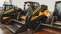 Man standing in front of 3 skid steer loaders.