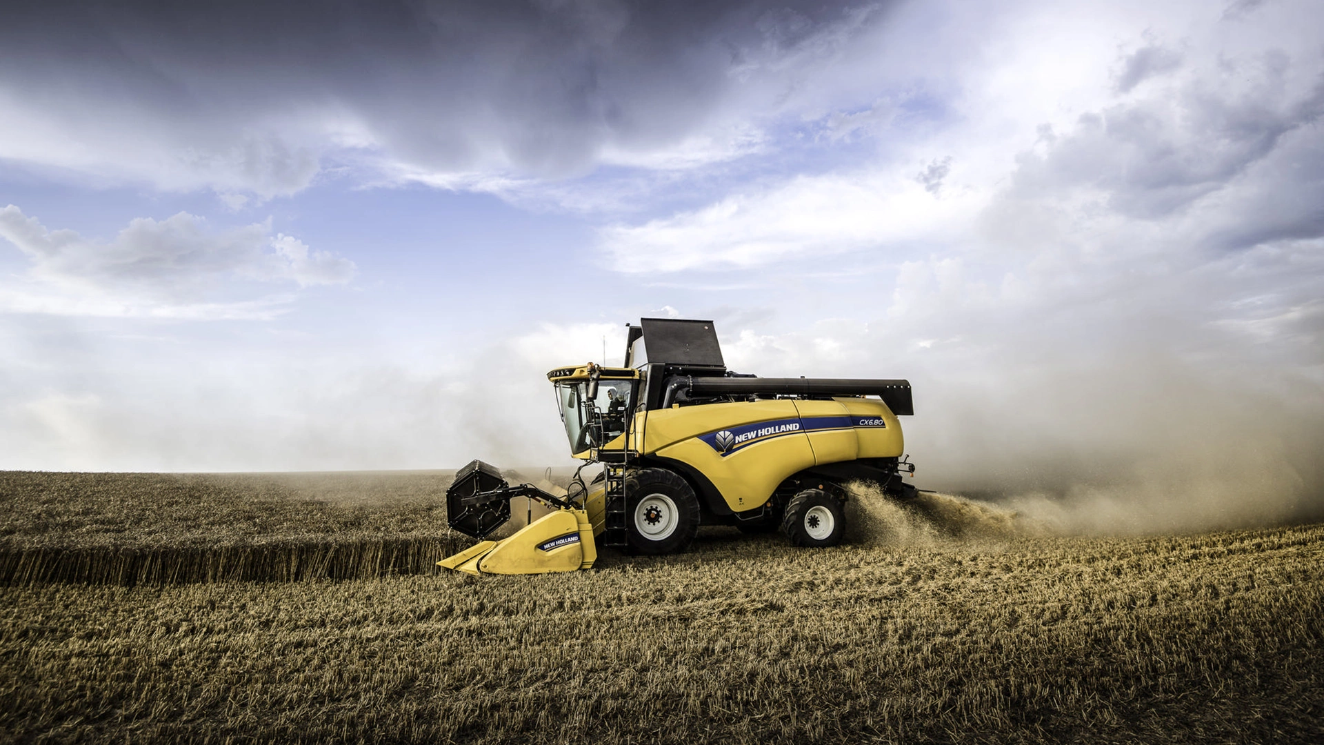 New Holland CX5-CX6 harvester cutting wheat, dust rising, golden field and cloudy sky backdrop.