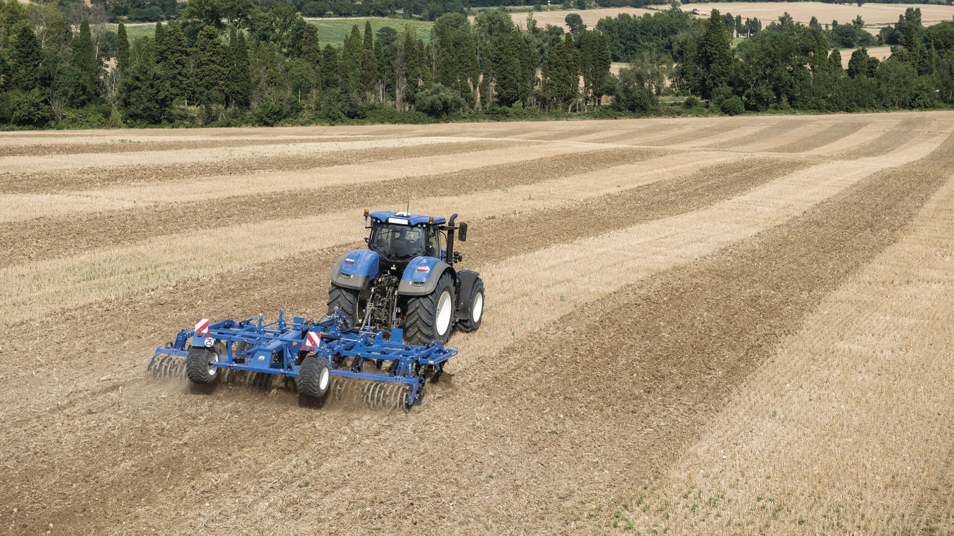 New Holland tractor employing a mounted stubble cultivator with rigid tine cultivator and rear rollers on the field