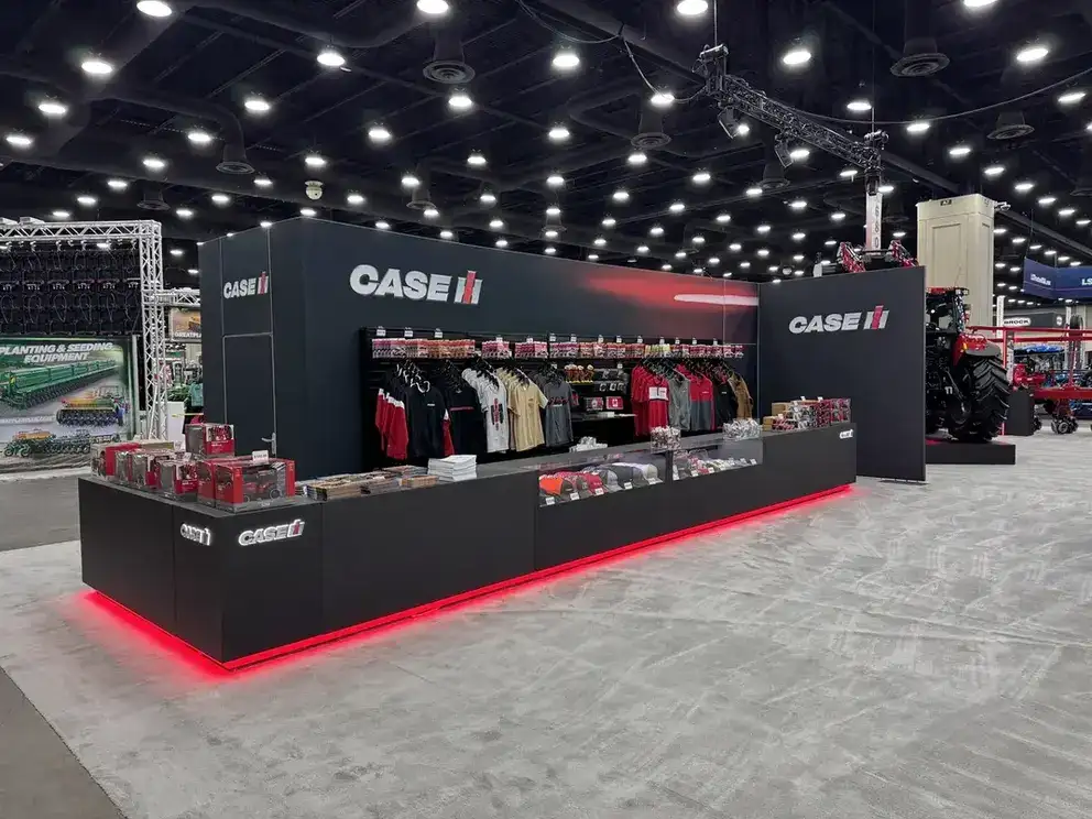 A trade show booth with Case IH branding displays merchandise like clothing and models. The black booth is illuminated with red neon, creating a sleek and modern look.