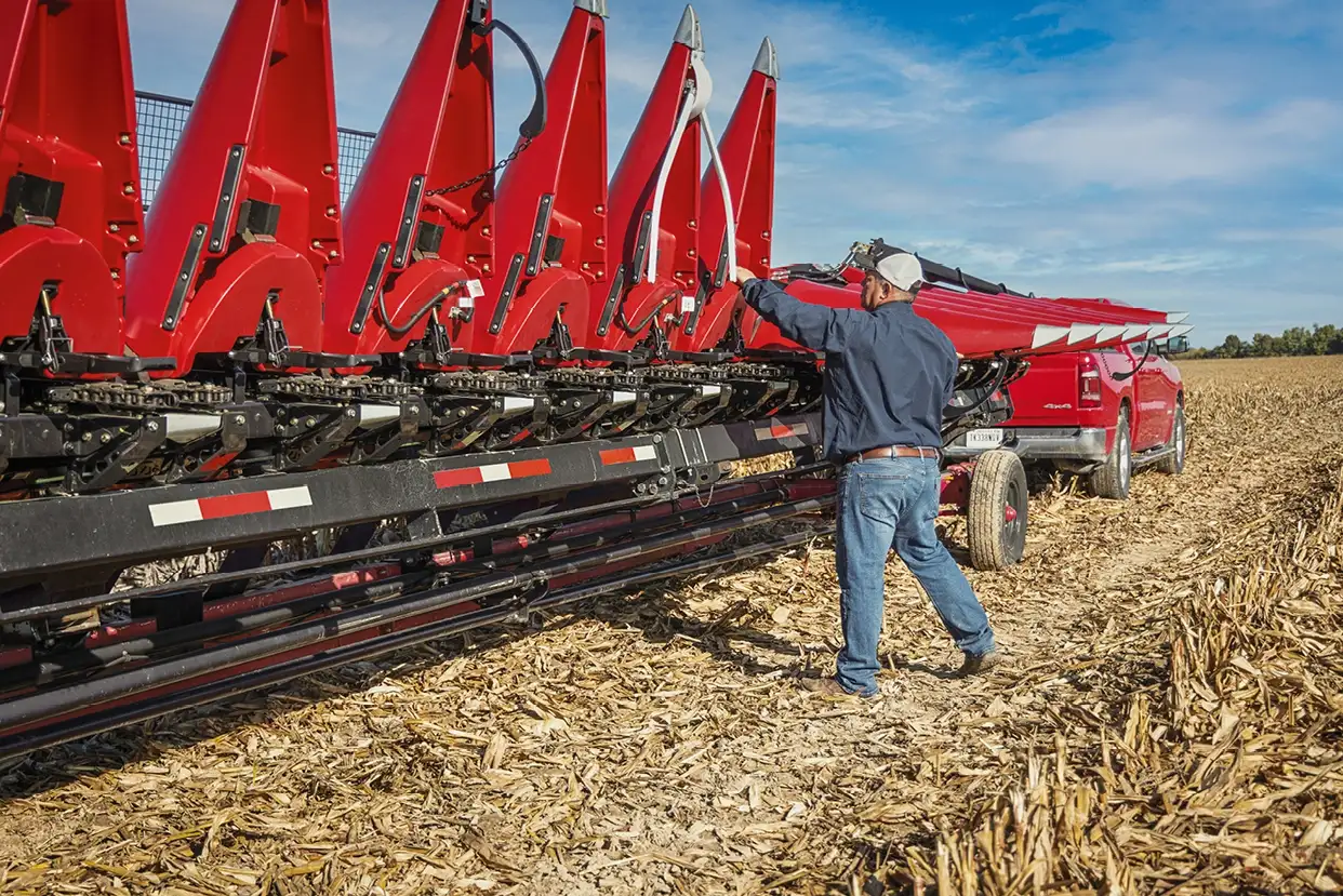 A farmer in a field adjusts a large Case IH C500 series agricultural machine attached to a truck.
