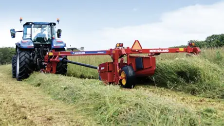Blue tractor mowing with red disc mower conditioner in a field.