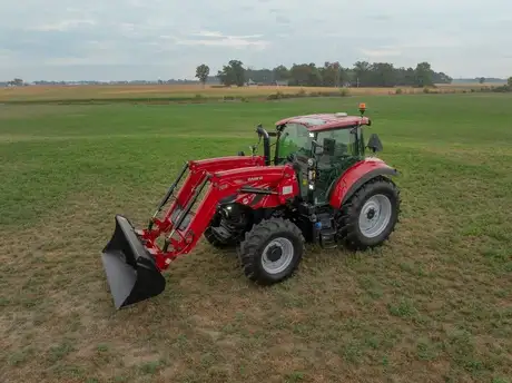 Case IH 120 Super M tractor with a front loader L113 attachment sits on a grassy field under a cloudy sky.
