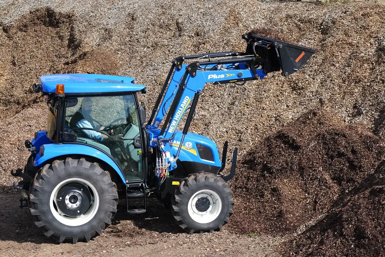 Blue New Holland TT4 Tier 3 tractor in field with loader and 4 in 1 bucket attached