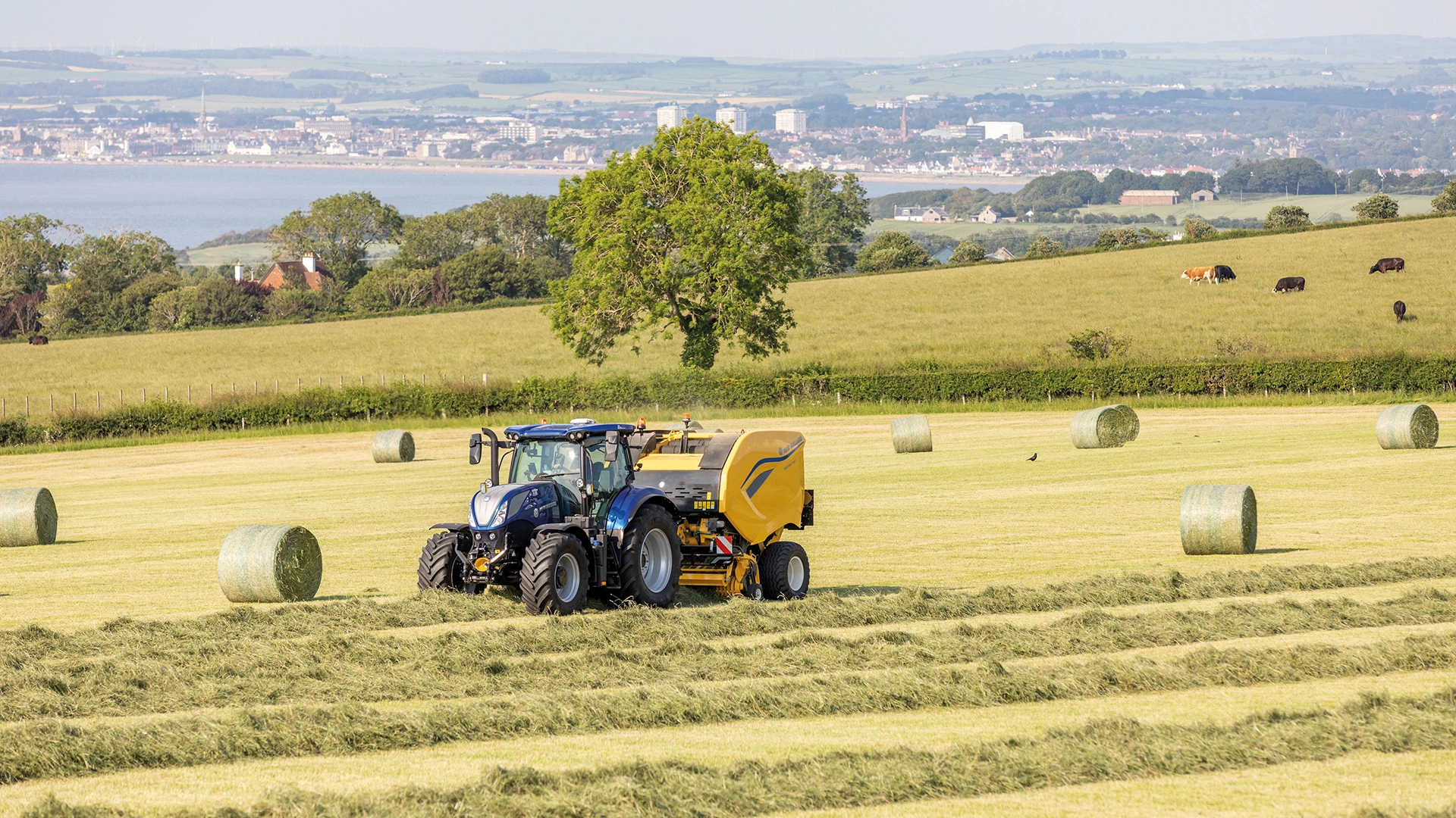 Farm tractor and Pro Belt round baler working in tandem, baling hay in the field