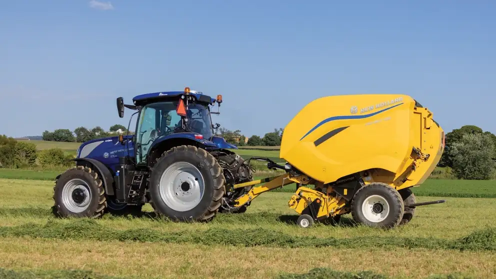 New Holland T7 tractor pulls a yellow Roll-Belt round baler.
