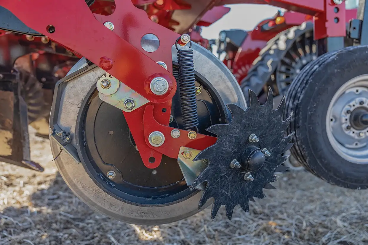 Close-up of a Case IH Nutri-Tiller 1000 toolbar showing a gauge wheel, spiked row cleaner, and spring on a red frame.