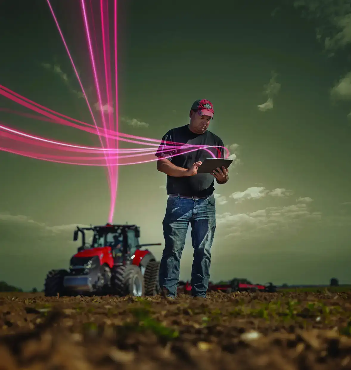 A farmer stands in a field using a tablet, with a Case IH tractor behind him. 