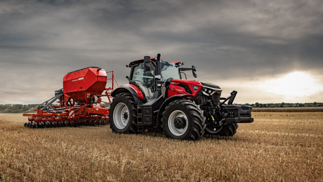 Red Case IH tractor with a seed drill in a stubble field under a cloudy sky at sunset.