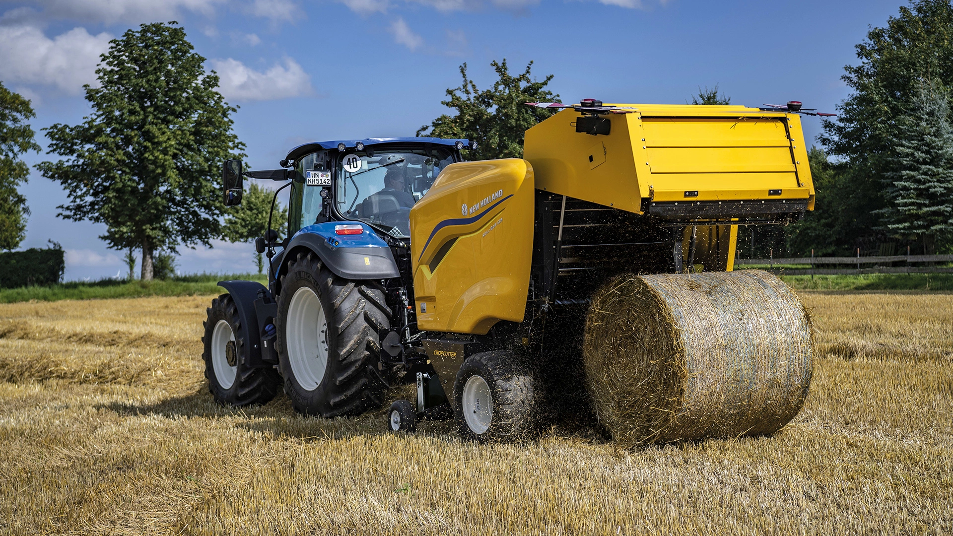 New Holland Tractor working with Roll Bar 125 round baler on an agricultural field.