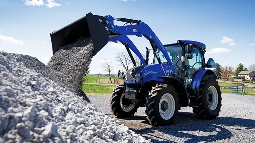Blue tractor dumping rocks into a pile.