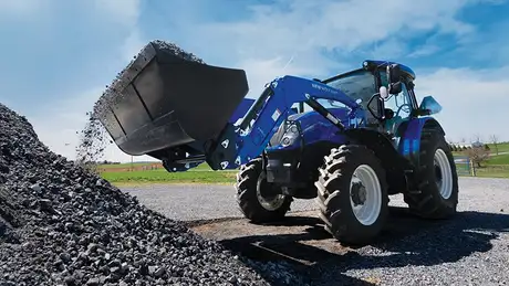 Blue tractor dumping rocks into a pile.