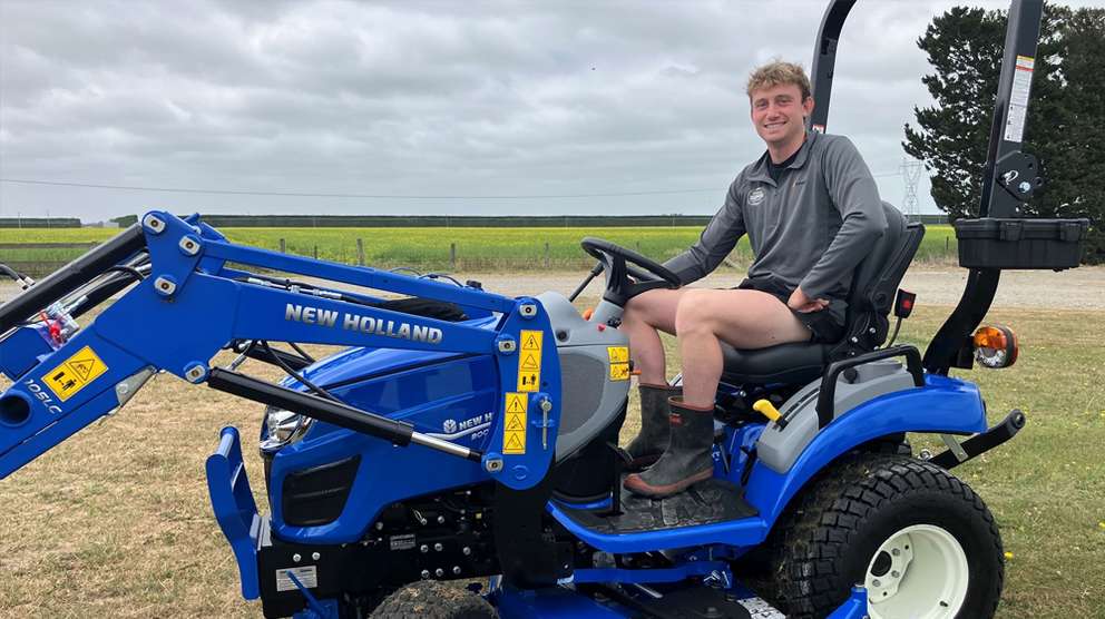 New Holland young farmer sitting inside blue tractor