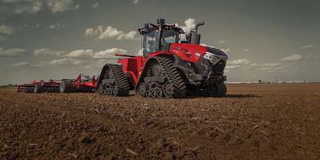 A large Case IH Steiger Quadtrac tractor equipped with tracks pulls a tillage implement across a wide, open field.