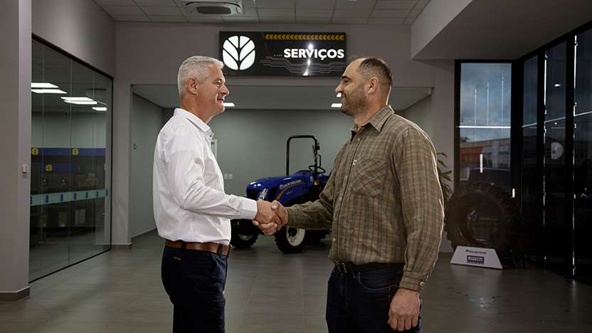 Cliente e consultor New Holland apertando as mãos em concessionária, simbolizando confiança e parceria nos serviços oferecidos.