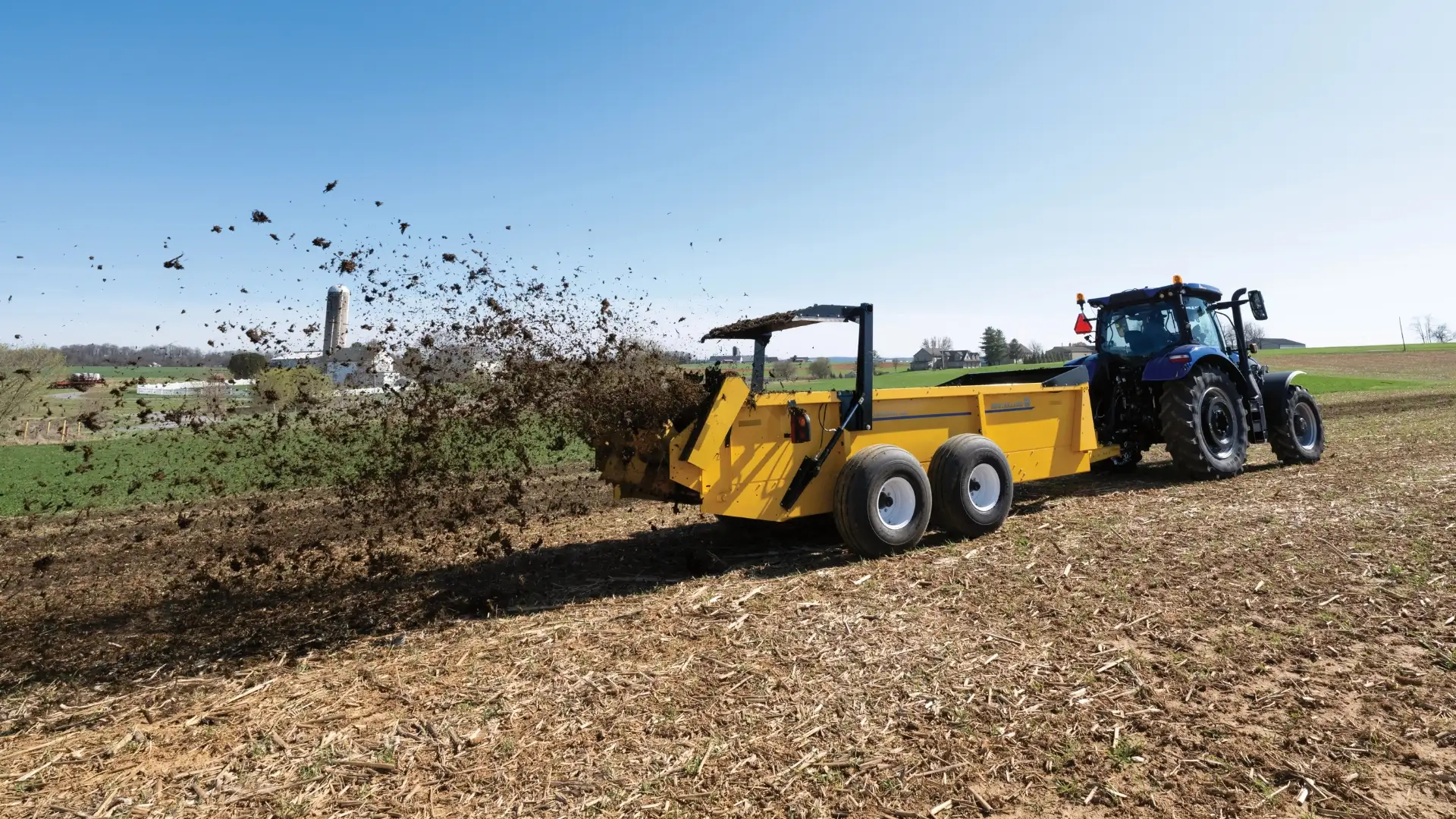 A yellow tractor spreads manure in a field.