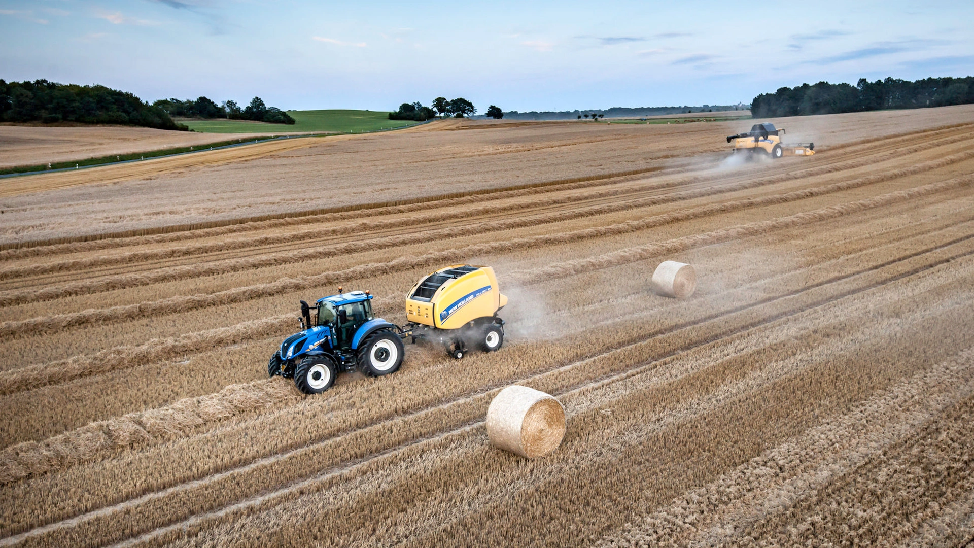 Tractor in action, operating a Roll-Belt round baler on an expansive agricultural field