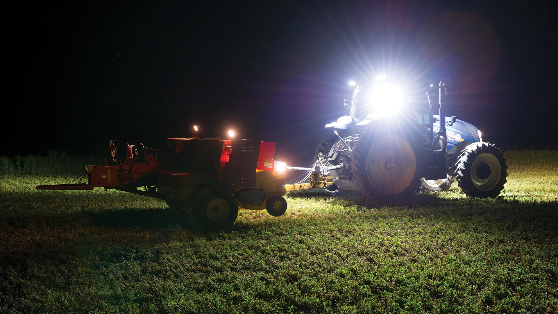 Tractor pulls a Hayliner® Small Square Baler at night