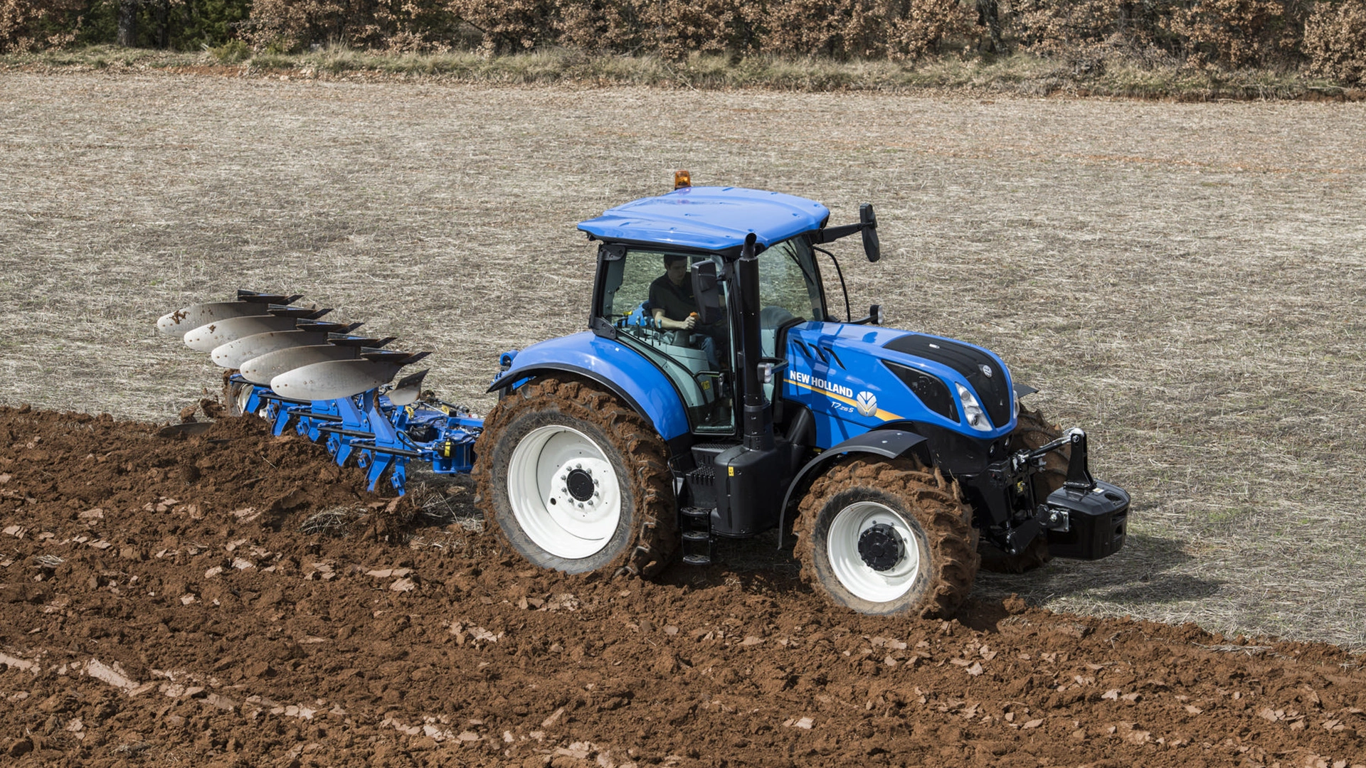 Tractor with a 5 furrow fully-mounted variable width reversible plough working on the field