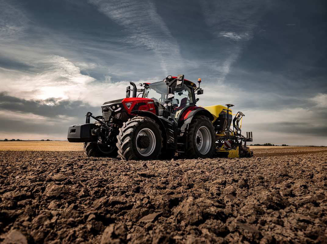 Red Case IH Puma 185 tractor with front weights and a yellow rear implement on plowed farmland.