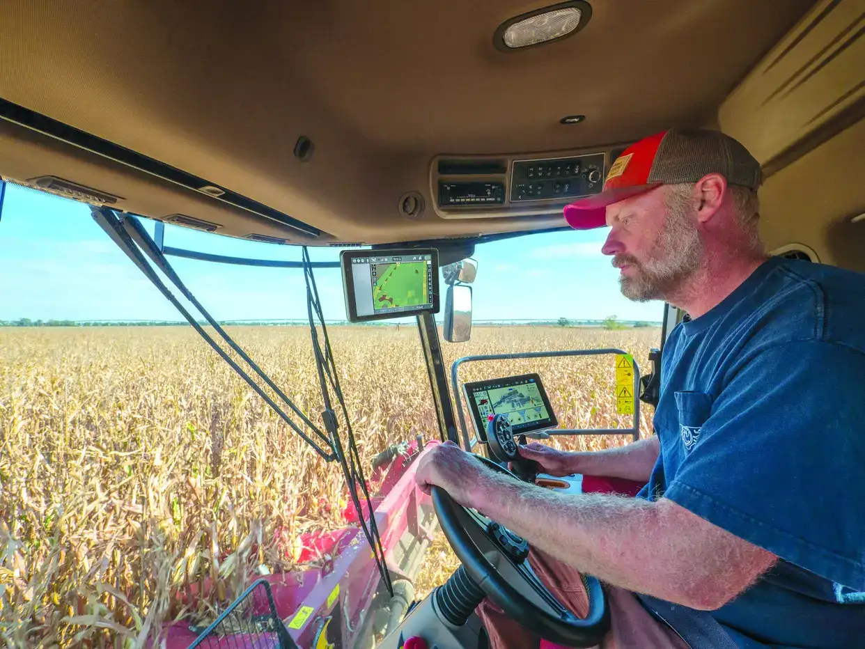 Farmer operating a modern Case IH combine harvester in a cornfield, using digital controls and navigation screens.