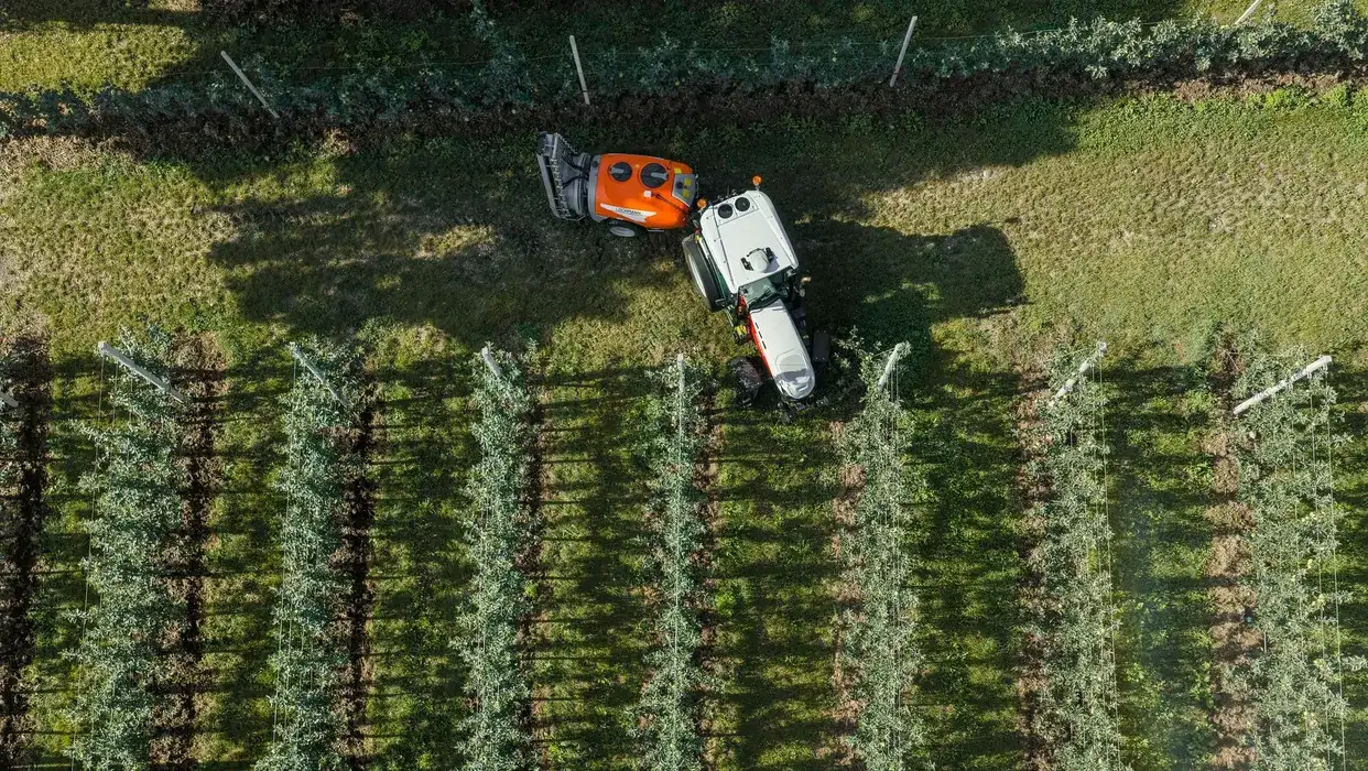 Overhead view of a STEYR Spezial orchard tractor with an orange sprayer working between rows of apple trees