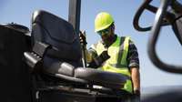 Man in yellow hard hat and vest next to seat of construction equipment.