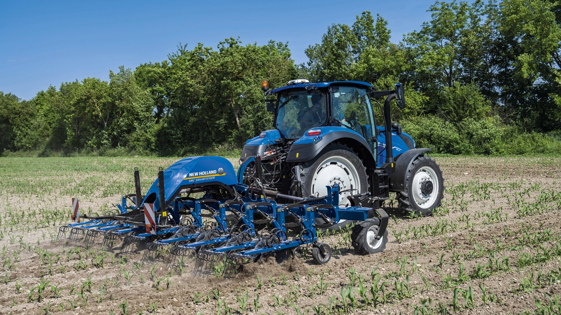 Tractor on a farm field, equipped with SRC & SRC SmartSteer Interrow Cultivators, tilling the soil between crop rows