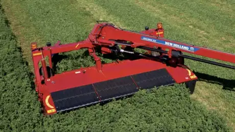 Red disc mower-conditioner mowing in a field.