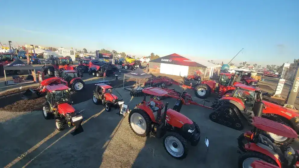 Outdoor agricultural equipment expo showcasing numerous red tractors on gravel with a clear blue sky. A large tent in the background displays "Case IH."